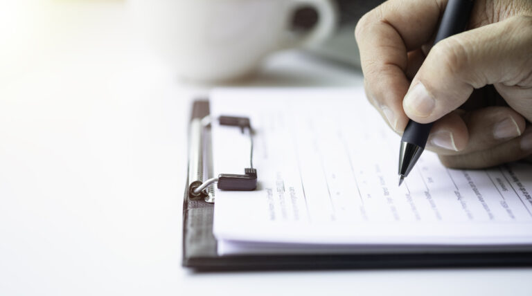 Close-up of Hand using writing pen with questionnaire or paperwork survey question filling in business company personal information form checklist document.